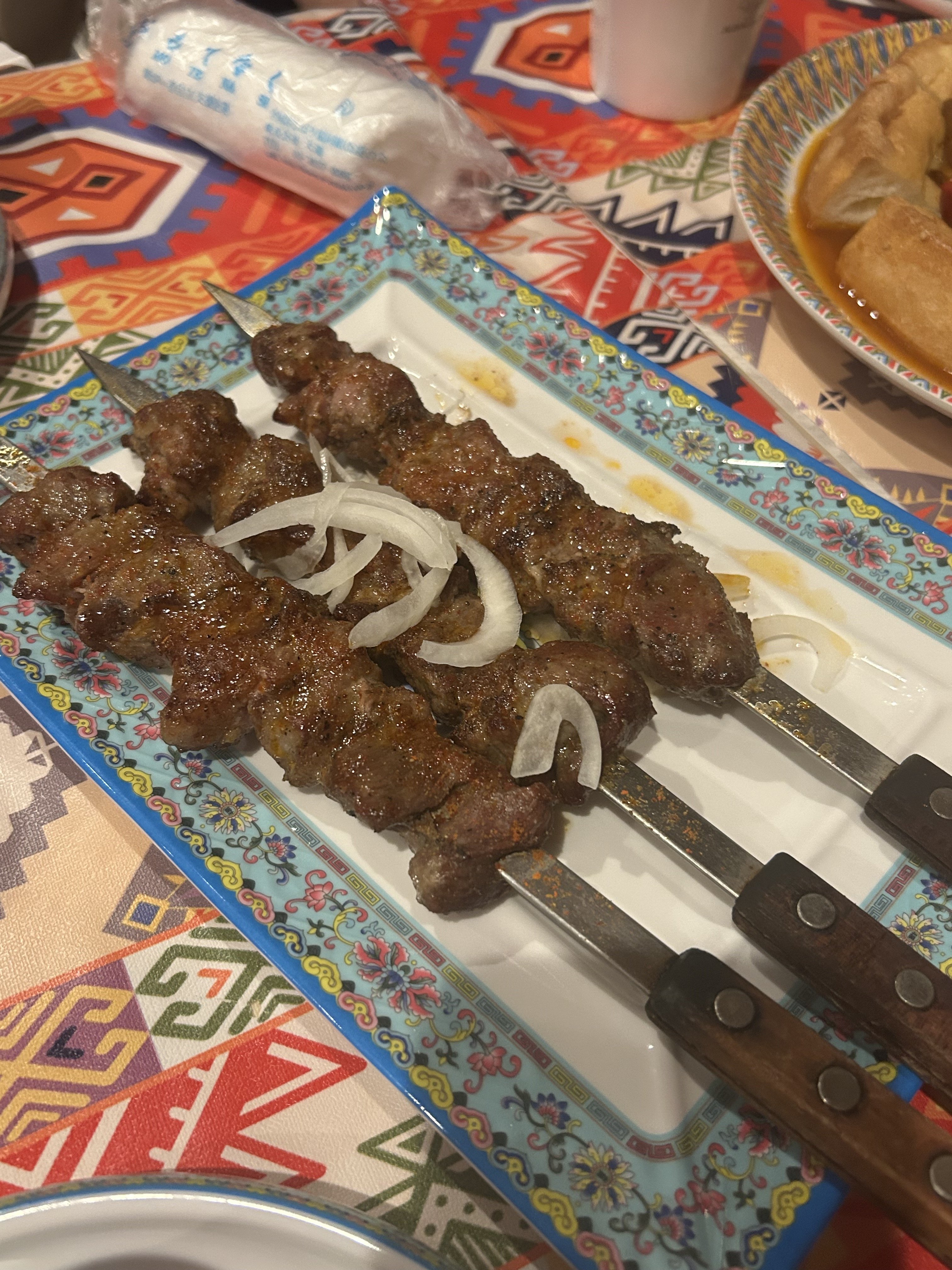 アリババのシシケバブ大。長串の羊肉ブロックを炭火で焼き上げた、玉ねぎスライス添えのウイグル風ラム串