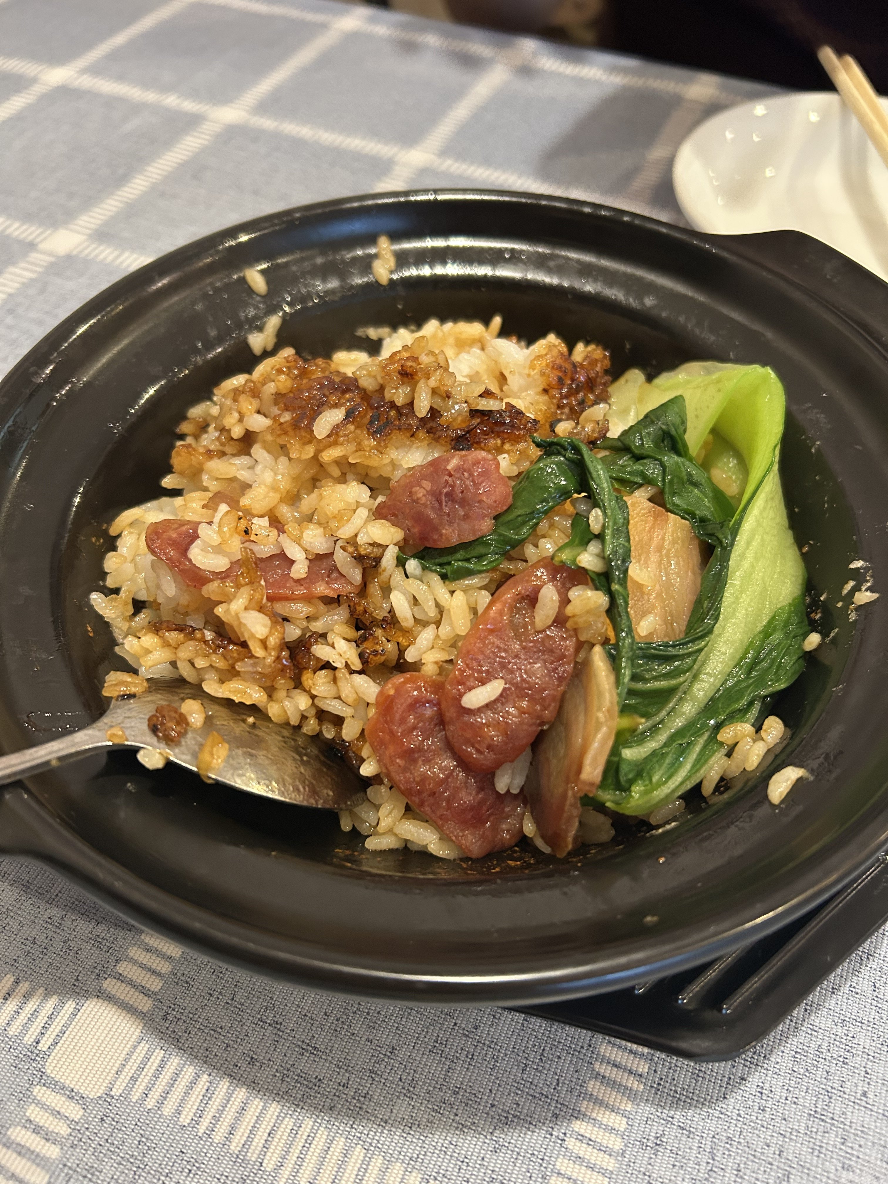 唐家の煲仔饭（土鍋ご飯）。黒い土鍋に中華腸詰（臘腸）と青菜、底にカリッと焼かれた香ばしいおこげ